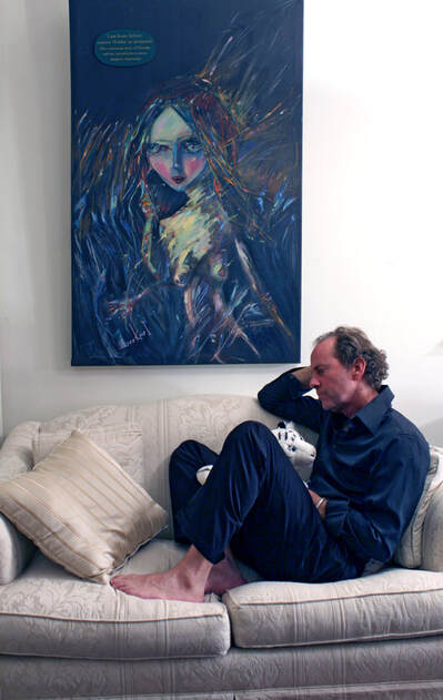 Michael, the artists, sitting on a couch in front of his painting, 